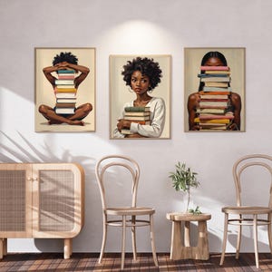 May include: Set of three framed art prints featuring illustrations of Black women with stacks of books. One print shows a woman sitting cross-legged with books covering her face. Another shows a woman holding books. The third shows a woman with books covering her face.