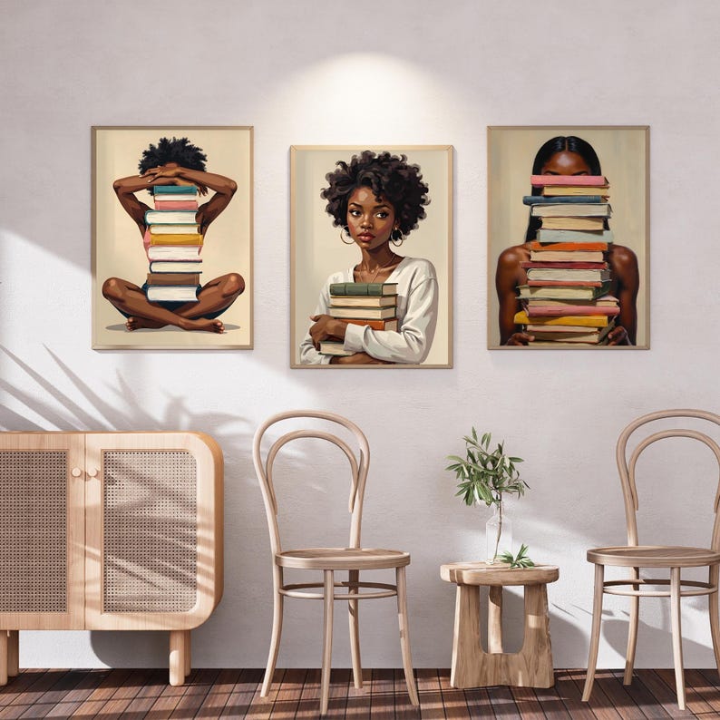 May include: Set of three framed art prints featuring illustrations of Black women with stacks of books. One print shows a woman sitting cross-legged with books covering her face. Another shows a woman holding books. The third shows a woman with books covering her face.