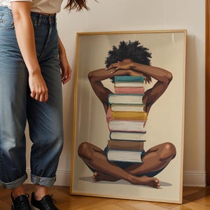 May include: A framed art print featuring a seated figure with arms crossed over the head, with a stack of books forming the body. The artwork has a neutral background and a wooden frame. The figure is depicted with dark skin and curly hair.