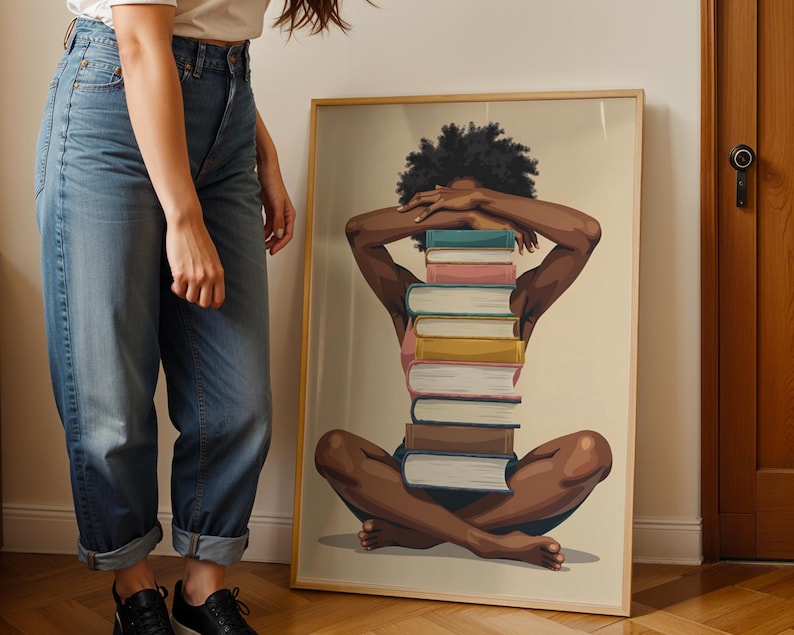 May include: A framed art print featuring a seated figure with arms crossed over the head, with a stack of books forming the body. The artwork has a neutral background and a wooden frame. The figure is depicted with dark skin and curly hair.