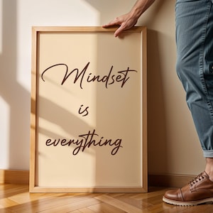 May include: A framed print with the words "Mindset is everything" in a stylish, cursive font. The frame is a light wood color, and the background is a soft beige. The print is leaning against a wall.