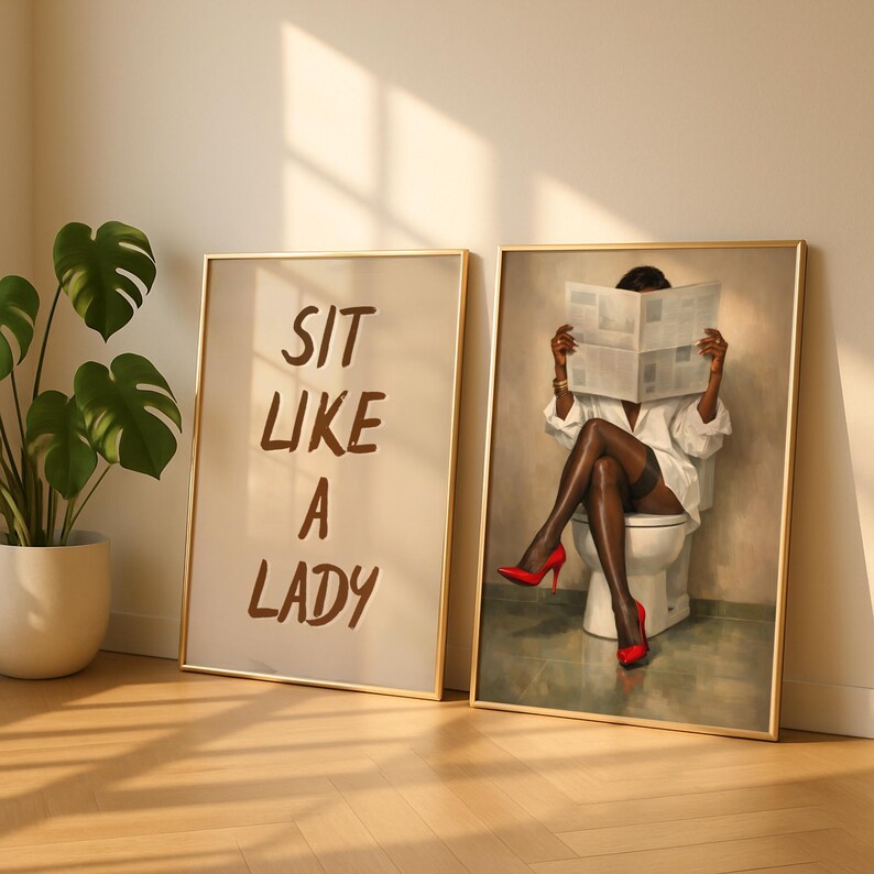May include: Two framed art prints. One print reads "SIT LIKE A LADY" in brown text. The other print depicts a person in a white shirt, black stockings, and red heels, reading a newspaper while seated on a toilet.
