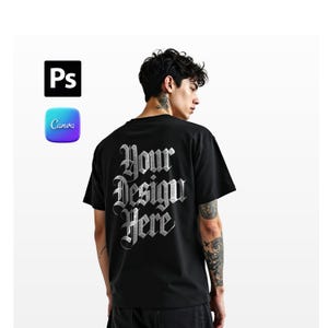 Może przedstawiać: Czarny t-shirt z napisem "Your Design Here" srebrną gotycką czcionką. Koszulka jest z krótkim rękawem. Logo Adobe Photoshop i Canva znajdują się w lewym górnym rogu.