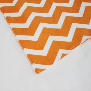 May include: Close-up of a corner of orange and white chevron fabric. The fabric has a white background with orange chevron stripes.
