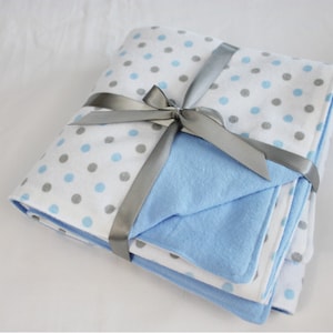 May include: A set of two baby blankets, one blue and one white with gray polka dots, tied together with a silver ribbon.