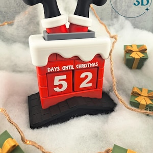 May include: A red chimney-shaped Christmas countdown calendar with Santa's legs sticking out. The calendar displays "52" days until Christmas. The chimney sits on a black roof, surrounded by small green gift boxes with gold bows.
