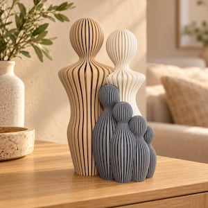 May include: A set of five abstract sculptures featuring vertical slats and rounded heads. The tallest figure is light tan, the second is off-white, and the three smaller figures are dark gray. Each piece has a ribbed, layered construction.