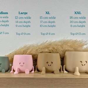 May include: Four matte-finish planters in sage green, light pink, tan, and beige, each featuring a smiling face cutout and two small legs. Text above lists sizes from Medium to XXL with dimensions in cm, including width, depth, height, and top diameter.