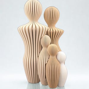 May include: A group of five abstract figures of varying heights, constructed from vertical, light-colored, ribbed slats. The figures are arranged in a cluster, with two taller figures in the back and three smaller figures in the front, creating a layered, sculptural composition with a consistent, repeating linear texture throughout.