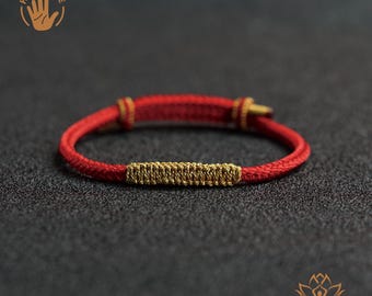 May include: Red bracelet with gold-colored accents. The bracelet features a woven gold-colored center section and gold-colored details at each end. The bracelet is handmade.