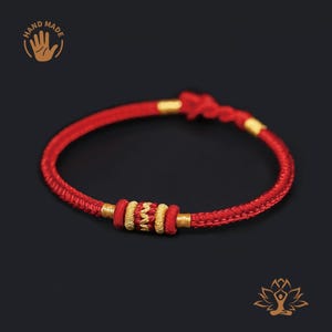 May include: Red braided bracelet with gold-colored accents. The bracelet features a central design of gold and red beads. The image includes the text "HAND MADE" and a hand graphic.