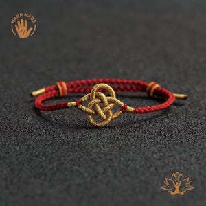 Puede incluir: Pulsera roja y dorada hecha a mano con un diseño de nudo dorado central. La pulsera está hecha de cordón rojo trenzado con detalles dorados y un cierre de nudo corredizo. La imagen incluye un logotipo "HAND MADE".