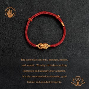 Puede incluir: Pulsera roja hecha a mano con un dise&ntilde;o de nudo dorado. La pulsera est&aacute; hecha de un cord&oacute;n rojo tejido con detalles dorados. La pulsera se muestra sobre un fondo oscuro. Se incluye el texto "HAND MADE".