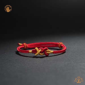 May include: Red and gold knot bracelet. The bracelet features a central knot design in gold, with red cord forming the rest of the bracelet. The bracelet is handmade.
