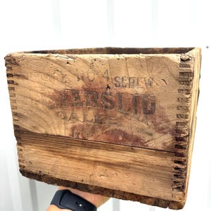 Puede incluir: Una caja de madera rectangular con esquinas de unión dentada y una textura desgastada. El panel frontal presenta texto oscuro estampado que dice NO 4 SCREW, VERSLIP y CALKS. La madera muestra vetas naturales, nudos y signos de envejecimiento.