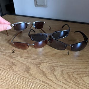 May include: An assortment of four pairs of sunglasses with different frame and lens styles. The sunglasses have various frame colors, including silver, brown, and black. The lenses are tinted in shades of brown and black.