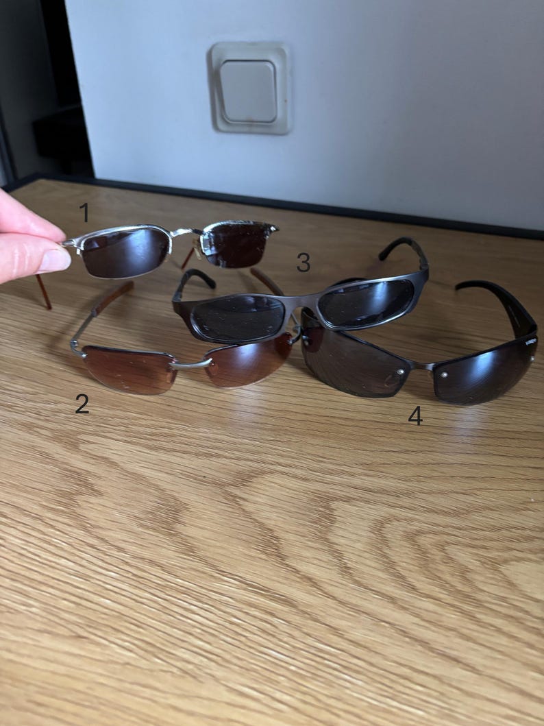 May include: An assortment of four pairs of sunglasses with different frame and lens styles. The sunglasses have various frame colors, including silver, brown, and black. The lenses are tinted in shades of brown and black.