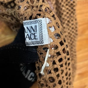 May include: Close-up of a brown, open-weave fabric with a label that reads "ANNI ACE" in a checkered frame. The fabric has a perforated design. The label also says "MADE IN ITALY".
