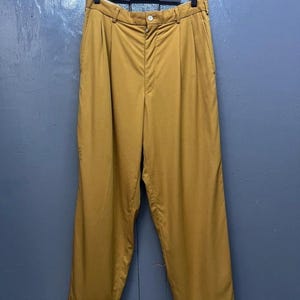 Puede incluir: Un pantal&oacute;n de color amarillo mostaza con pliegues, cierre de bot&oacute;n y pierna recta.