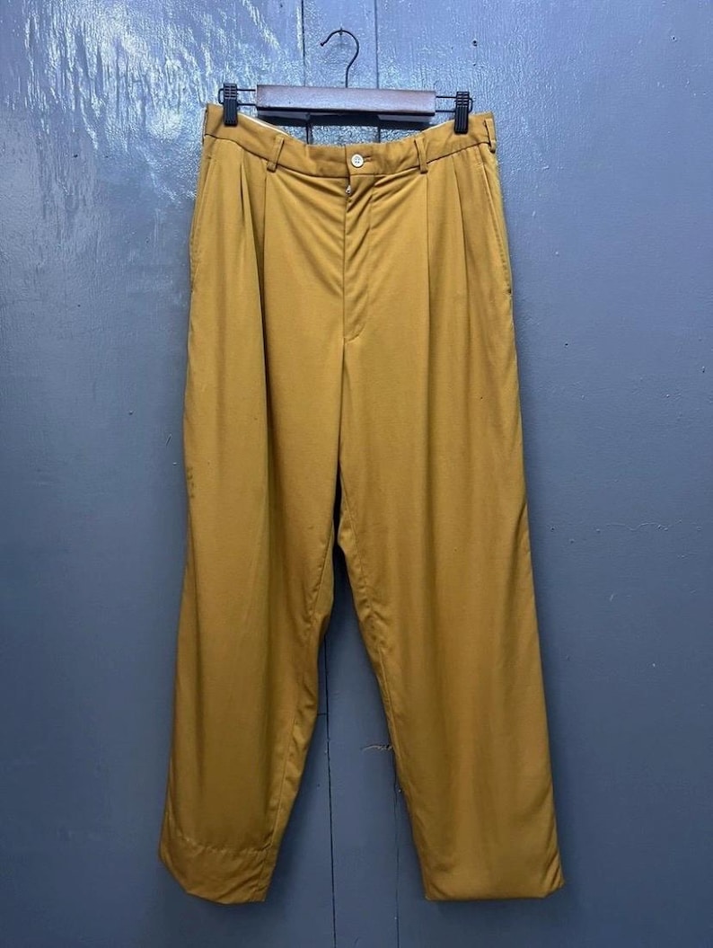 Puede incluir: Un pantal&oacute;n de color amarillo mostaza con pliegues, cierre de bot&oacute;n y pierna recta.