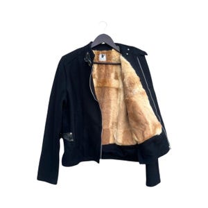 May include: Black jacket with a faux fur lining. The jacket has a zipper closure and a small pocket on the front. The interior lining is a light brown color. The jacket is hanging on a black hanger.