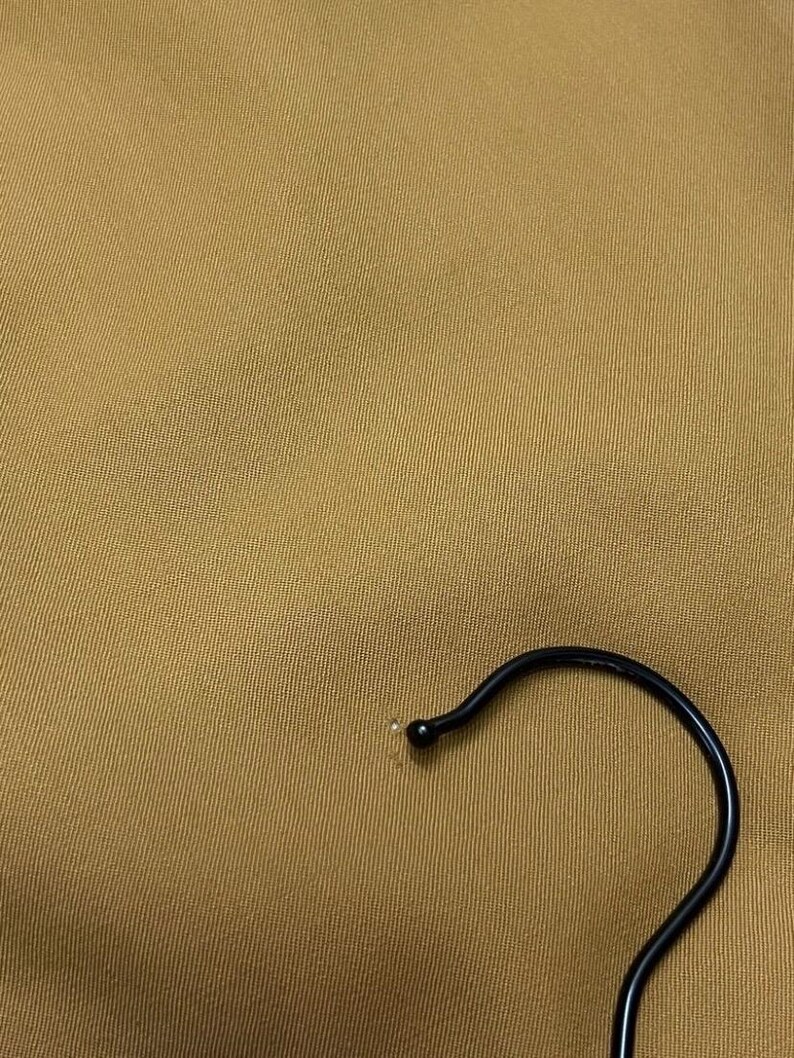 Puede incluir: Primer plano de una tela marr&oacute;n con un gancho de percha de metal negro.