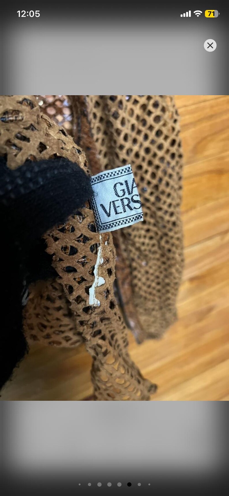 May include: Close-up of a brown, open-weave garment with a black accent. A tag with the text "GIA VERS" is attached. The garment appears to be made of a textured material, possibly leather or a similar fabric.