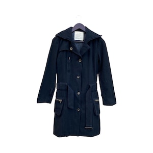 May include: A black wool coat with a wide collar, button closure, and a belt. The coat has two front pockets with zippers and is hanging on a black hanger. The coat is a mid-length style.