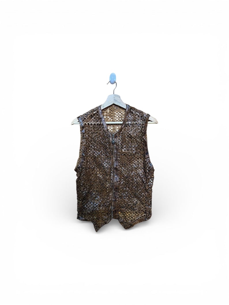 May include: A brown, open-weave vest with a zipper closure, hanging on a wooden hanger. The vest has a textured, patterned design and a V-neck. The garment is displayed against a white background.