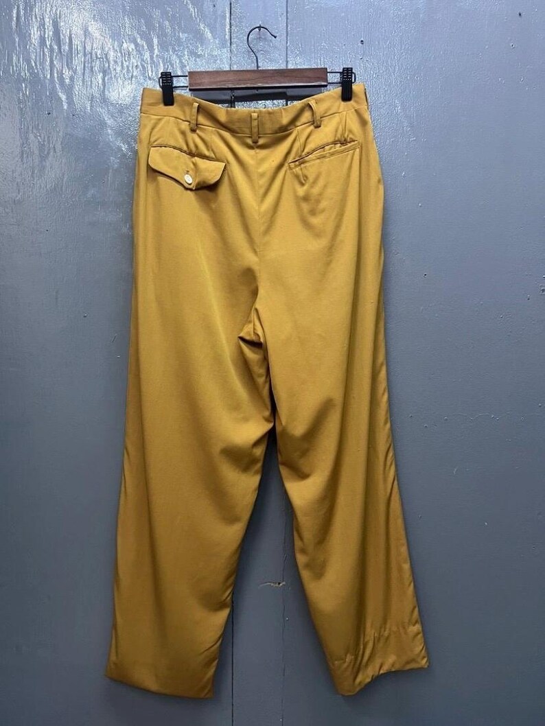 Puede incluir: Un pantal&oacute;n de pierna ancha de color mostaza con un bot&oacute;n en el bolsillo trasero.