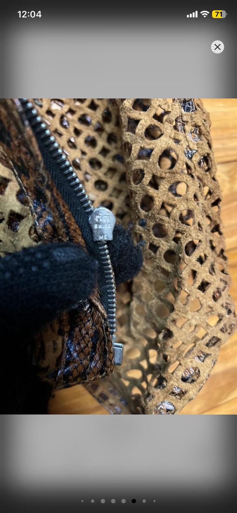 May include: Close-up of a brown and tan leather garment with a zipper. The zipper pull is silver and has the text "riri SWISS ME". The garment has a cut-out design and a snakeskin pattern.