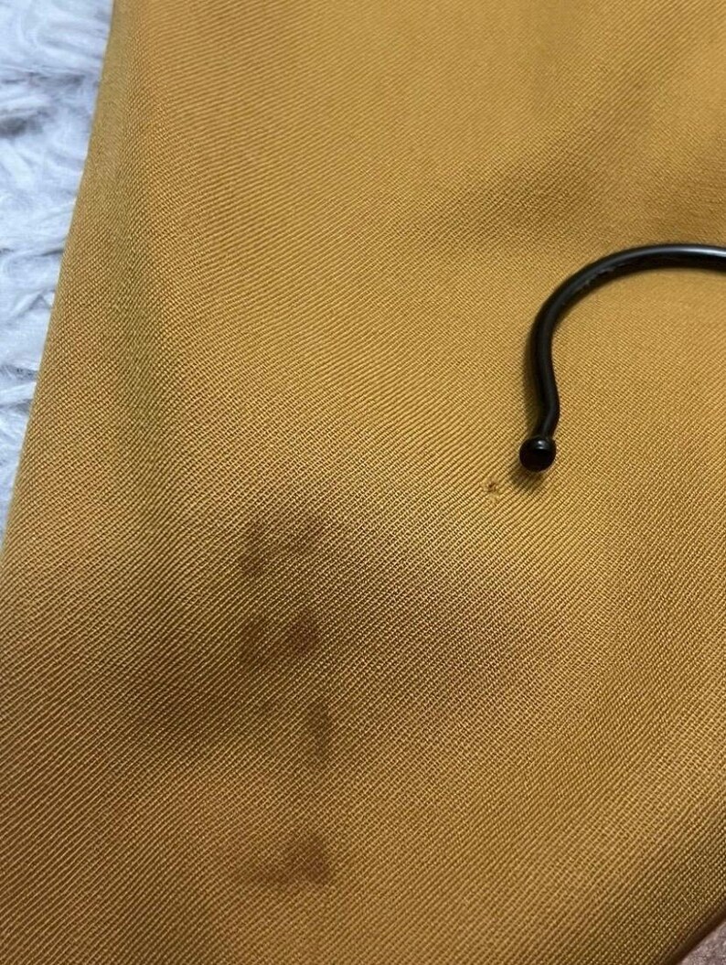 Puede incluir: Primer plano de una tela de color amarillo mostaza con una textura sutil. La tela tiene una mancha oscura en el centro.