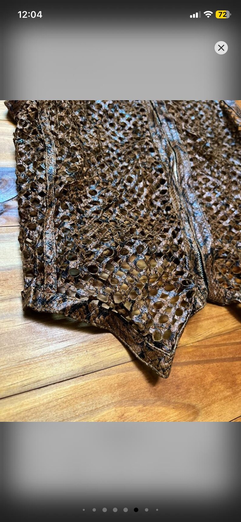 May include: Close-up of a brown, open-weave garment with a textured surface. The garment has a zipper and is made of a material that resembles snakeskin. The item is likely a vest or jacket.
