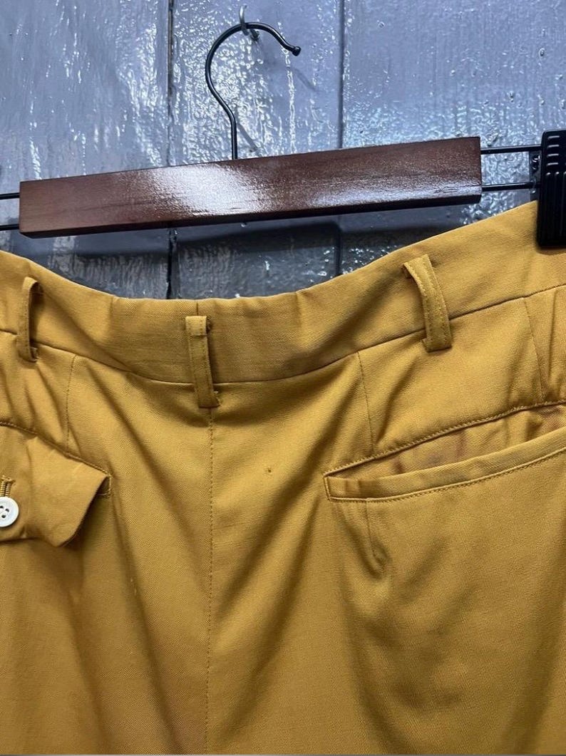 Puede incluir: Vista trasera de pantalones de color amarillo mostaza con un bot&oacute;n y un bolsillo en el lado izquierdo y un bolsillo en el lado derecho.