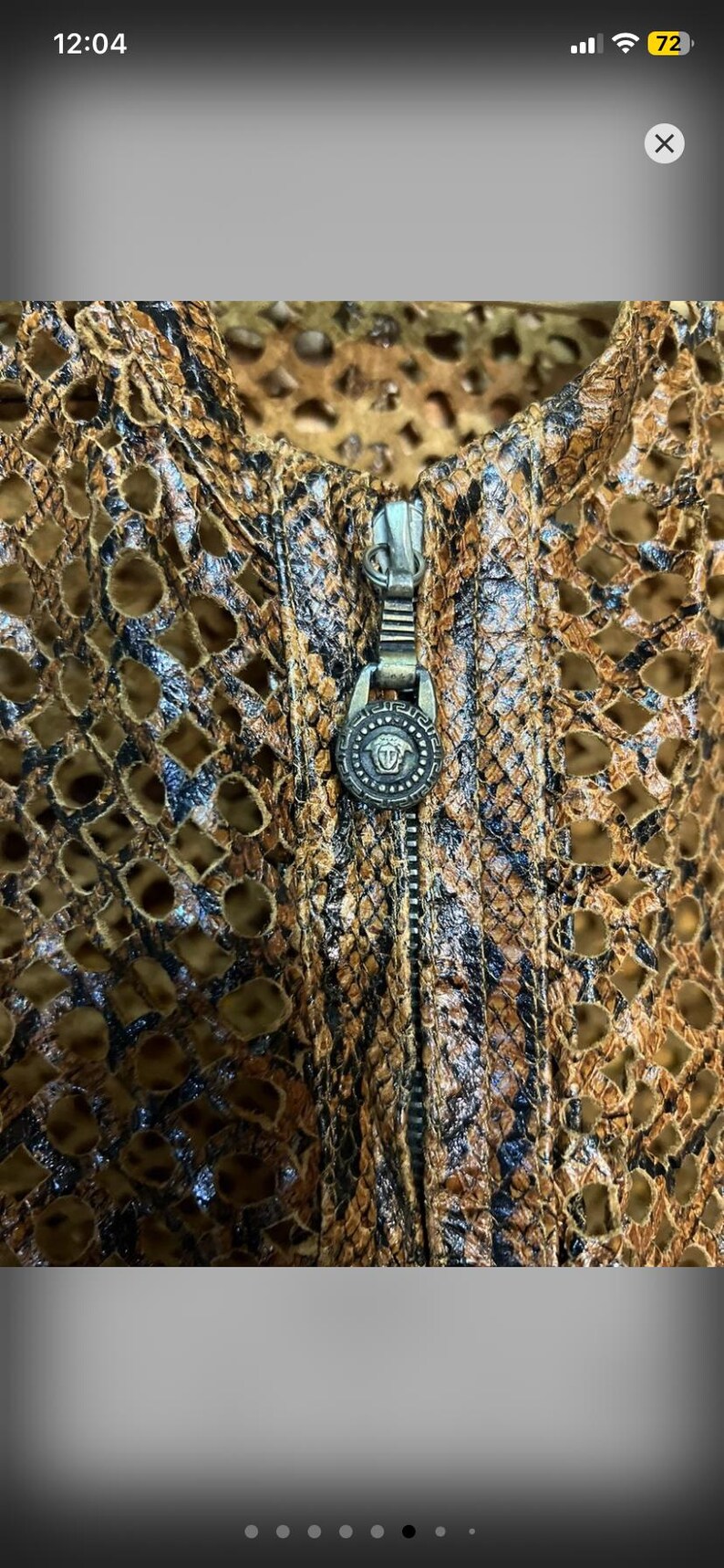 May include: Close-up of a brown and black patterned jacket with a zipper. The jacket has a unique design with cut-out details. The zipper pull features a decorative emblem.