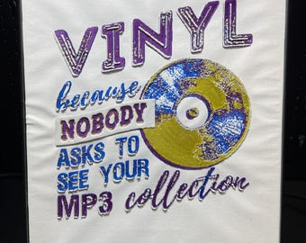 Pode incluir: Uma tela branca enquadrada com o texto "VINYL because nobody asks to see your MP3 collection" em bordado roxo e azul. Um grande disco de vinil bordado está no centro da tela.