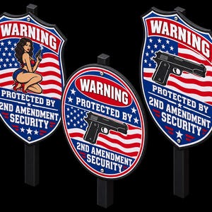 Könnte beinhalten: Drei Metallschilder auf schwarzen Pfosten mit dem Text WARNING PROTECTED BY 2ND AMENDMENT SECURITY. Zwei schildförmige Schilder zeigen eine amerikanische Flagge, eines mit einer Pin-up-Illustration und eines mit einer schwarzen Handfeuerwaffe.