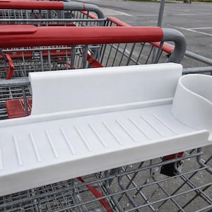 Puede incluir: Accesorio blanco de plástico para carrito de compras, con bandeja y portavasos. La bandeja tiene ranuras verticales y un borde elevado. Diseñado para acoplarse a un carrito.