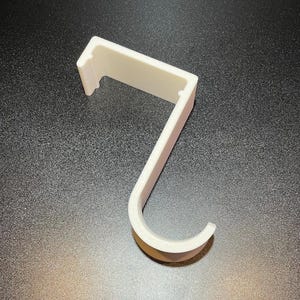 May include: A white plastic hook with a rectangular base and a curved hook. The hook is designed to hang items on a wall or other surface.