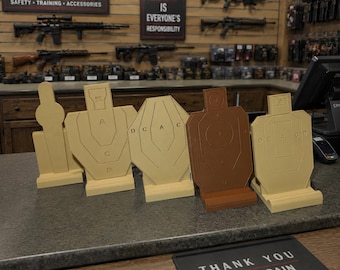 May include: A selection of paper shooting targets in various shapes and shades of beige and brown. They are displayed on a counter in a gun shop. The sign reads "Safety is Everyone's Responsibility."