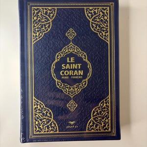 Peut inclure: Un livre relié en bleu avec des accents dorés et le titre "LE SAINT CORAN" en lettres dorées. Le livre est en arabe et en français.