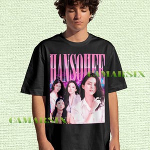 Könnte beinhalten: Schwarzes T-Shirt mit einer Grafik einer Frau und dem Namen "HANSOHEE" in rosa und lila Text. Die Grafik enthält mehrere Bilder der Frau. Das T-Shirt wird von einer Person getragen.