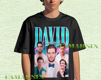 May include: Black t-shirt featuring a retro-style graphic of a man with the name "DAVID" in large, teal and white letters. The graphic includes multiple images of the man. The shirt is worn by a person.