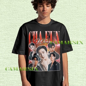 May include: Black t-shirt with a retro graphic design featuring Cha Eun Woo and the text "CHA EUN Woo". The design incorporates multiple images of the celebrity. The t-shirt has a crew neck.