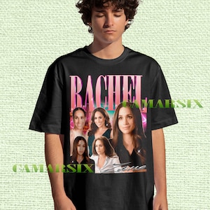 May include: Black t-shirt featuring a graphic of the name "RACHEL" in pink and white, with multiple images of a woman. The word "True" is printed below the images. The shirt is worn by a person.