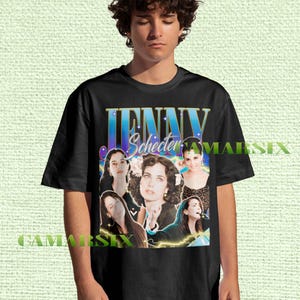 Puede incluir: Camiseta negra con un diseño gráfico que presenta el nombre "JENNY Schecter" en letras azules y doradas, con múltiples imágenes de una mujer. El diseño tiene un estilo vintage y retro.