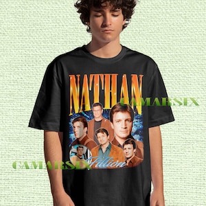 May include: Black t-shirt with a collage of images of Nathan Fillion, with the name "NATHAN" in large orange and yellow letters. The shirt also includes the name "Fillion" in a blue script font.