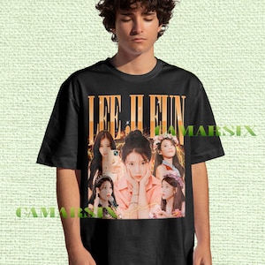 May include: Black t-shirt featuring a graphic design with the text "LEE JI EUN" in orange and white. The design includes multiple images of a woman. The shirt is made of a soft material.