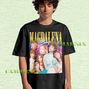 May include: Black t-shirt featuring a colorful graphic of the band Magdalena Bay. The design includes the band's name in gold lettering and multiple images of the band members. The shirt is a classic crew neck style.