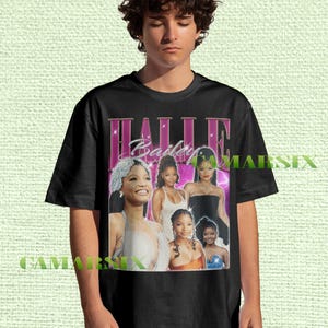 May include: Black t-shirt featuring a collage of images of Halle Bailey with the text "HALLE Bailey" in a pink and white retro design. The shirt has a classic crew neck and short sleeves.